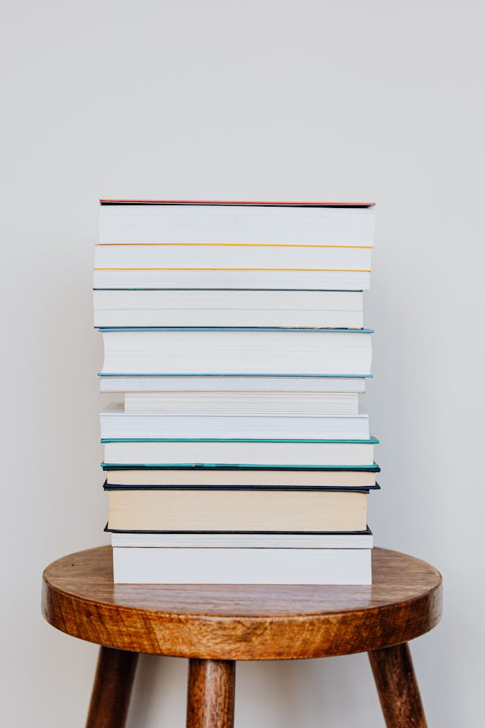 pexels-photo-4219041 A neat stack of books placed on a rustic wooden stool, perfect for reading scenes.