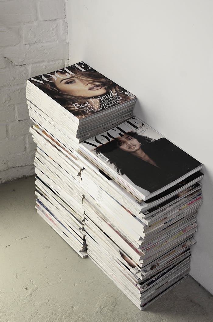 pexels-photo-6045028 High angle many fashion magazines stacked on floor against white brick wall in studio